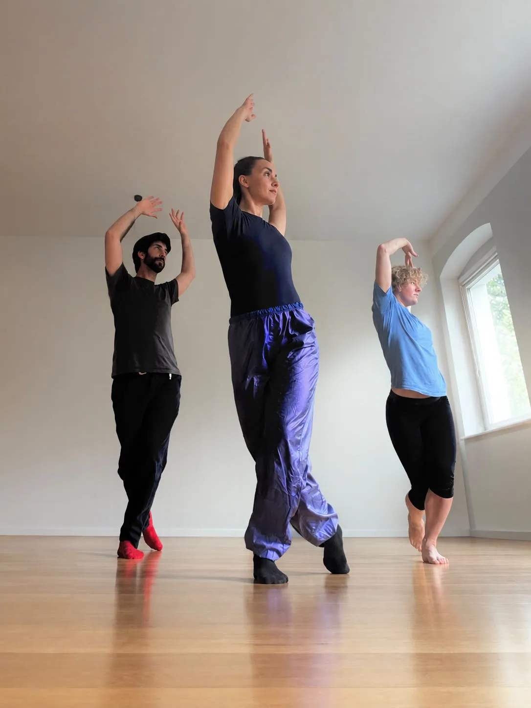 Lucy and two students holding a modern dance pose with arms raised in a bright studio